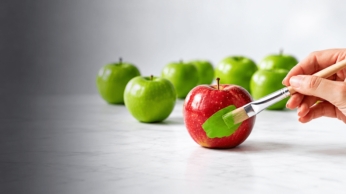 Manzana roja pintada de verde junto a varias manzanas verdes